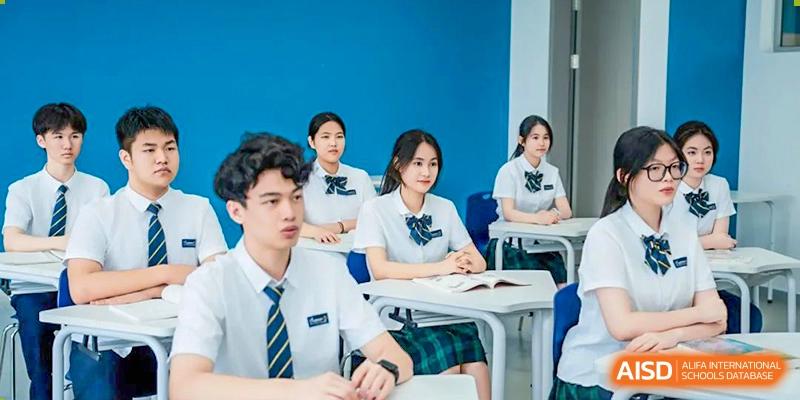 Students wearing uniforms with ties and seated at desks are attentively listening to a lesson in a bright classroom at Ardingly College Zhongshan (ACZS), focusing on academic concentration.