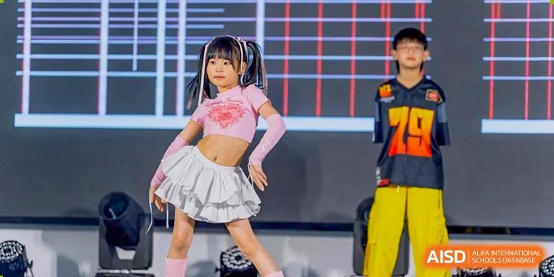 A young female student in a pink, two-piece outfit is performing a vibrant dance routine on stage at Ardingly College Zhongshan (ACZS), showcasing talent and extracurricular arts programs.