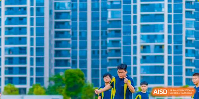A student in a blue and yellow uniform stands outside a tall, modern building, representing the urban environment and the contemporary campus facilities of Ardingly College Zhongshan (ACZS).