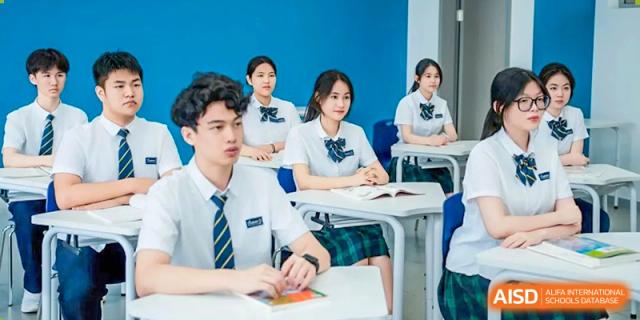 A male and several female students in uniform are seated at desks, engaged in a lesson in a bright classroom at Ardingly College Zhongshan (ACZS), emphasizing academic focus.