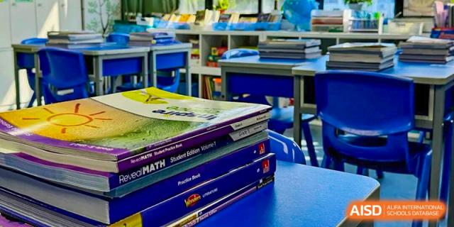 A stack of colorful student textbooks and math workbooks sits ready on a blue classroom desk at Korea International School in Shenzhen.