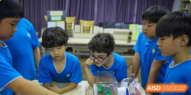 Two young students in blue shirts look curiously at a science project model displayed on a table in a classroom at Korea International School in Shenzhen.