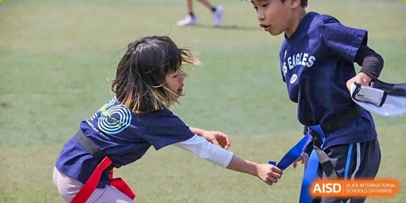 A young girl in a blue shirt reaches out during a sports activity on a grassy field at Korea International School in Shenzhen.
