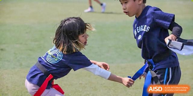 A young girl in a blue shirt reaches out during a sports activity on a grassy field at Korea International School in Shenzhen.