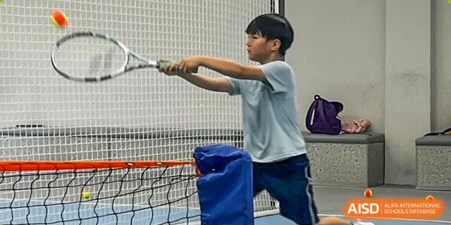 A young boy focuses on his form while practicing his swing with a racquet on a court at Korea International School in Shenzhen.