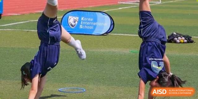 Students participate in outdoor athletics near a blue school banner on the track and field at Korea International School in Shenzhen.