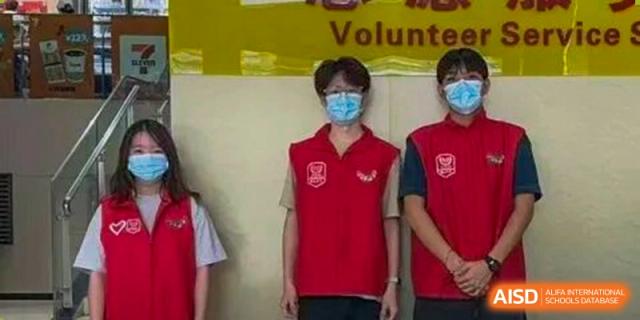 Two staff members wearing red volunteer vests and face masks stand together indoors at Korea International School in Shenzhen.