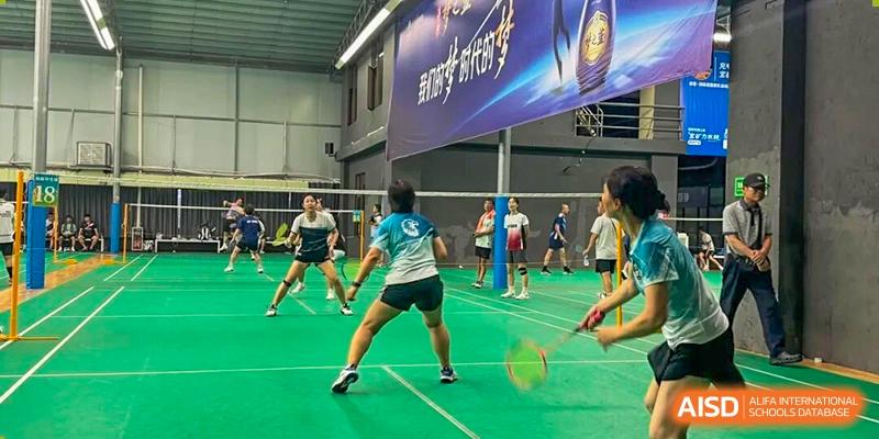 Students in athletic gear play a competitive game of badminton on a green indoor court at Korea International School in Shenzhen.