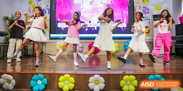 Two young girls in dresses perform a dance routine on a stage decorated with yellow flowers at Korea International School in Shenzhen.