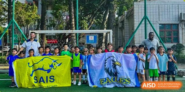A group of students proudly display a yellow school flag and a blue "Eagles" banner on the soccer pitch at Korea International School in Shenzhen.
