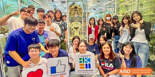 A large group of students and staff pose together while holding signs and giving thumbs-up gestures at Korea International School in Shenzhen.