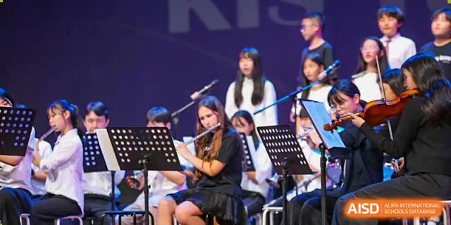 A student musician sits on stage and plays the flute during a live orchestral performance at Korea International School in Shenzhen.