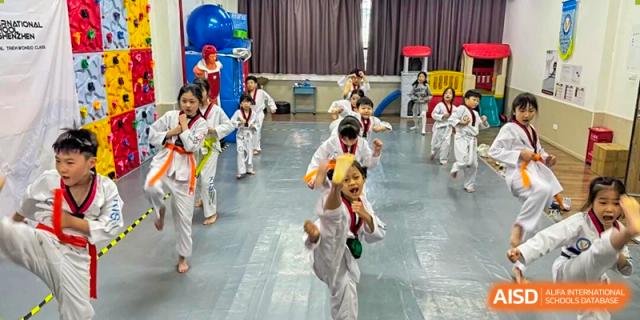 A young student in a white uniform performs a high front kick during a Taekwondo class in the gymnasium at Korea International School in Shenzhen.