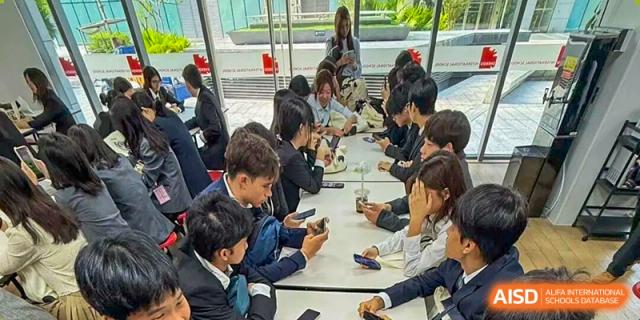 A group of students sit together at long white tables outdoors during a social break or study session at Korea International School in Shenzhen.