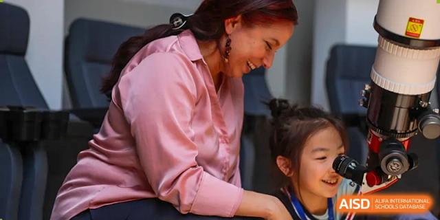 A teacher smiling and assisting a young student with their schoolwork in a supportive environment at BASIS International School Wuhan.