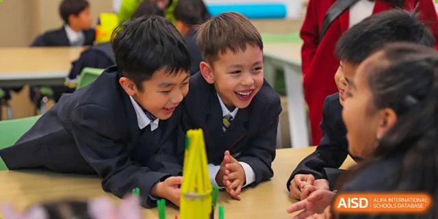 Two young students in formal school uniforms smiling and building a structure together with blocks at BASIS International School Wuhan.