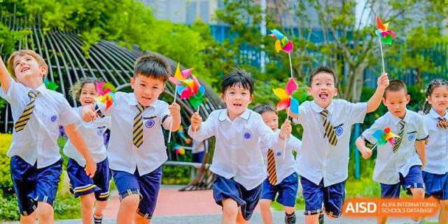Excited young students running outdoors while holding colorful pinwheels during a school activity at BASIS International School Wuhan.
