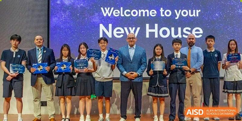 Students in uniform stand on stage with a faculty member holding awards in front of a "Welcome to New House" sign at BASIS International School Wuhan.