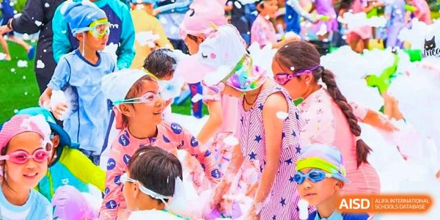 Excited children wearing swim caps, goggles, and colorful summer gear participate in a fun outdoor water or foam activity at BASIS International School Wuhan.