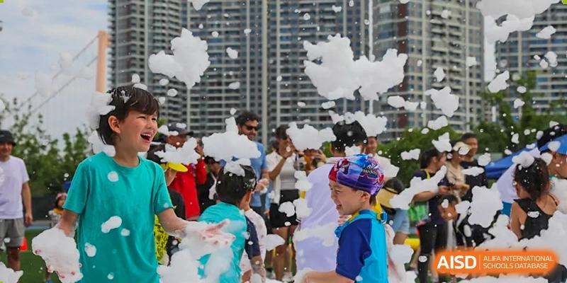 Children play joyfully in a large cloud of white foam during an outdoor school event at BASIS International School Wuhan.