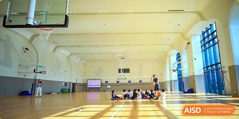 Students gather on the polished wood floor of a large, bright indoor gymnasium at BASIS International School Wuhan.