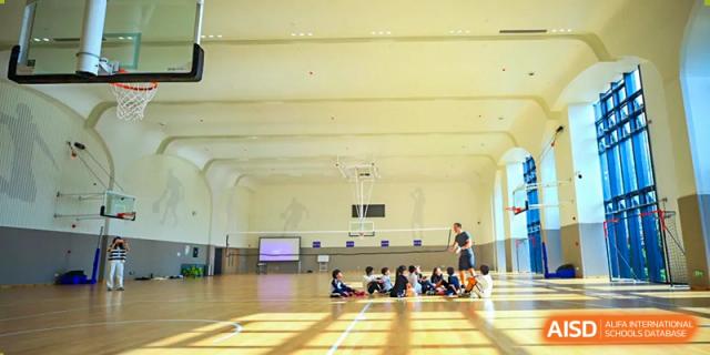 Students gather on the polished wood floor of a large, bright indoor gymnasium at BASIS International School Wuhan.
