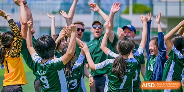Excited students and teachers in green athletic gear cheering and raising their hands at BASIS International School Wuhan.