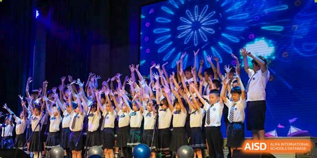 A large student choir performing on a stage with vibrant blue lighting and decorations at BASIS International School Wuhan.