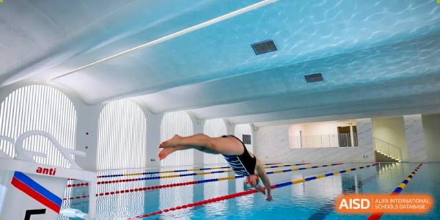 A student athlete mid-air performing a dive into the school's indoor swimming pool at BASIS International School Wuhan.