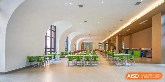 A wide, bright school cafeteria featuring modern white arched ceilings and green seating for students at BASIS International School Wuhan.