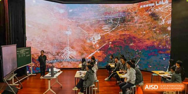 Students attend a lecture in a classroom with a large, abstract-looking display or board at Hangzhou Entel Foreign Language School. The students are seated facing the front.