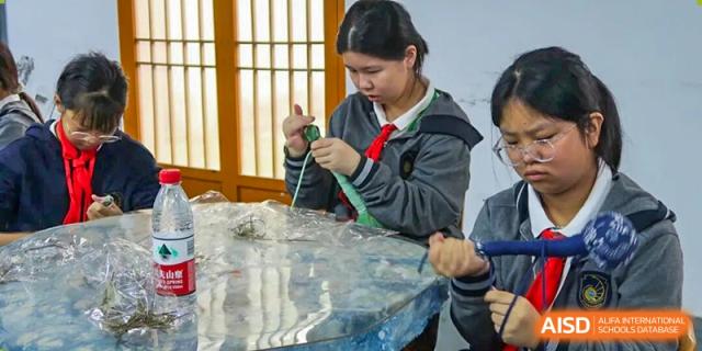 A student working on a craft or practical project, possibly involving sewing or weaving, at Hangzhou Entel Foreign Language School. The student is focused on the material.