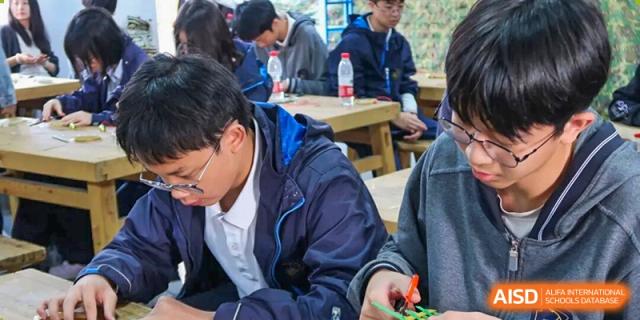 A student intently working on a small, hands-on activity or project at a table with other students at Hangzhou Entel Foreign Language School.