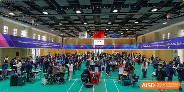 Large indoor sports hall event with many people seated, banners featuring Chinese and other flags visible, suggesting a competition or ceremony at Hangzhou Entel Foreign Language School.