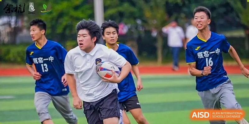 Two male students run aggressively side-by-side on a sports field, one carrying a ball and looking ahead, in a competitive moment during a game at Hangzhou Entel Foreign Language School.