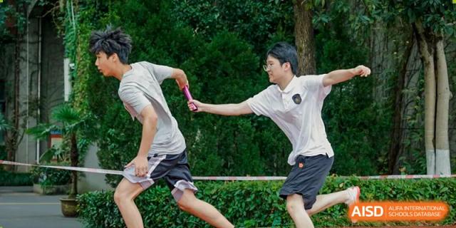 Two students run on a track during a relay race, exchanging a baton in a moment of fast action at Hangzhou Entel Foreign Language School.