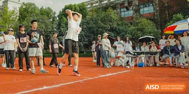 A student jumps high in the air during a long jump or high jump event on a red track, surrounded by spectators at Hangzhou Entel Foreign Language School.