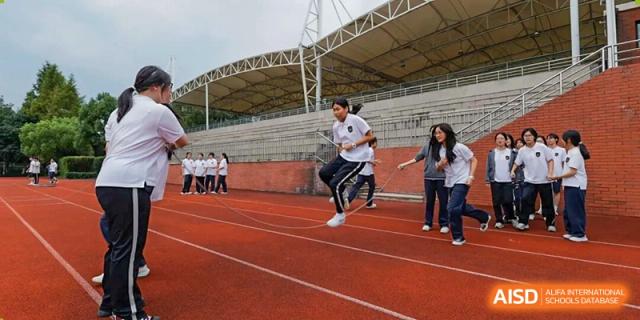 Students participate in a track and field event, one jumps over a low obstacle while others look on, inside a stadium at Hangzhou Entel Foreign Language School.