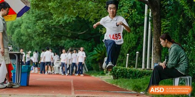 A student mid-air during a long jump event, wearing a number 1485 bib at Hangzhou Entel Foreign Language School sports day.