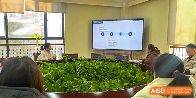 Indoor scene at Hangzhou Entel Foreign Language School showing a classroom with a large display screen and lush green plants in the foreground.