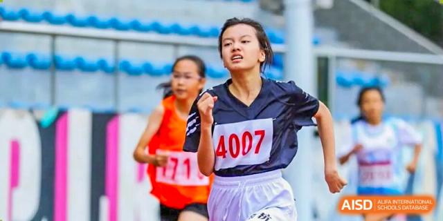 A determined female student from Hangzhou Entel Foreign Language School sprinting fiercely on the track during a race, wearing a navy and white sports uniform.