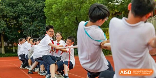 Students from Hangzhou Entel Foreign Language School participating in a team tug-of-war competition on the grass, working together during the fun school sports event.