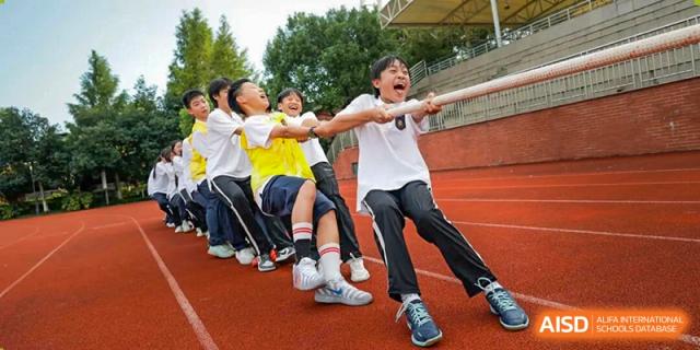 Energetic students from Hangzhou Entel Foreign Language School participating in a spirited tug-of-war competition on a sports field during an outdoor event.