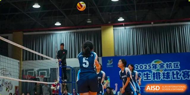 Hangzhou Entel Foreign Language School volleyball team members actively playing an indoor match, focusing on the ball and their positions on the court.