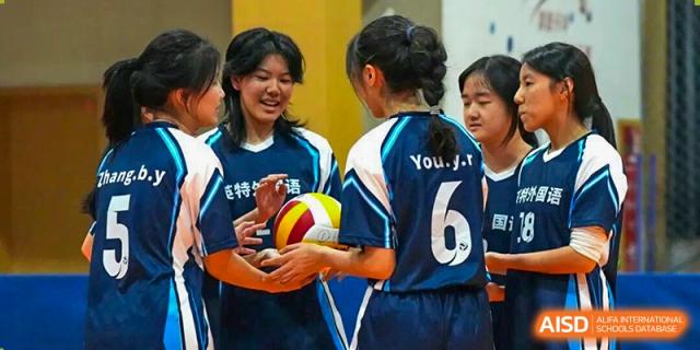 Hangzhou Entel Foreign Language School female volleyball players huddle together before a game, holding a ball, wearing matching blue team uniforms.
