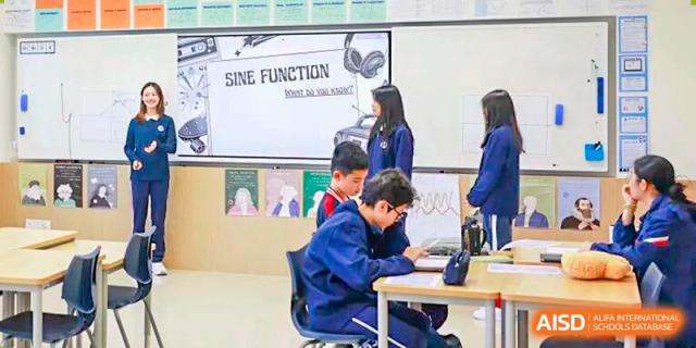 Students in uniform work on tablets at their desks, with a "SINE FUNCTION" math poster on the board at BASIS International School Park Lane Harbour.