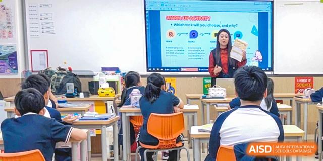 A teacher presents a lesson on a large screen to students seated in a modern classroom at BASIS International School Park Lane Harbour.