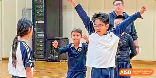 Two young boys in school uniforms cheer enthusiastically with their hands raised during a sports activity at BASIS International School Park Lane Harbour.