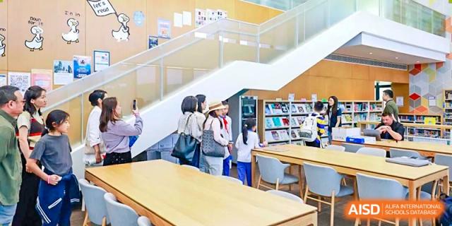 Students stand in a bright, modern library area with large windows, bookshelves, and tables at BASIS International School Park Lane Harbour.