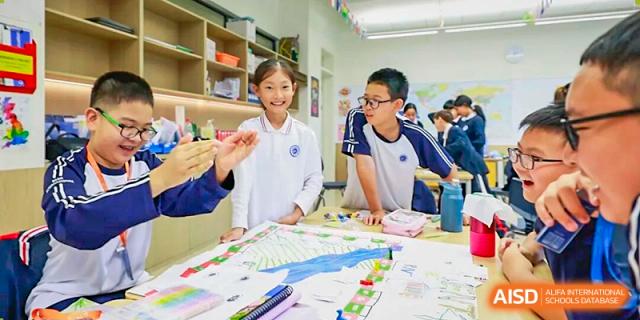 Two students happily present a large, detailed map or project to their classmates in a classroom setting at BASIS International School Park Lane Harbour.
